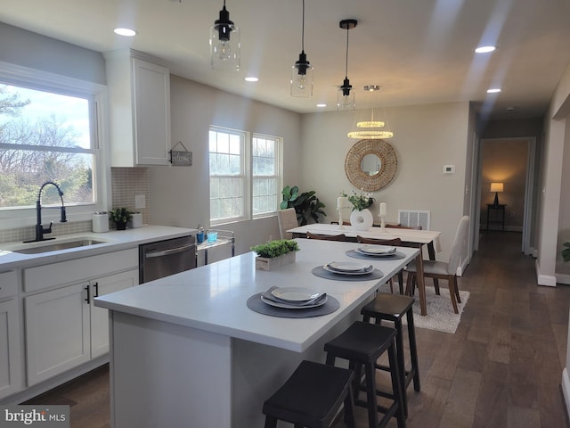 kitchen featuring light countertops, hanging light fixtures, white cabinetry, a kitchen island, and dishwasher