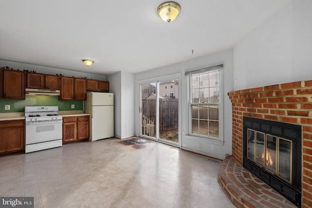 kitchen featuring white appliances, visible vents, light countertops, under cabinet range hood, and a fireplace