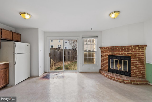 kitchen featuring brown cabinetry, a brick fireplace, freestanding refrigerator, and baseboards