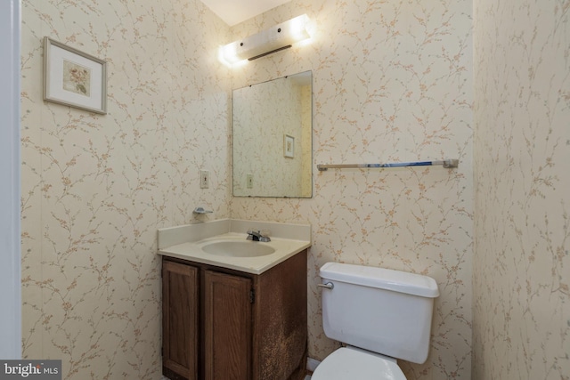 bathroom with toilet, wallpapered walls, and vanity