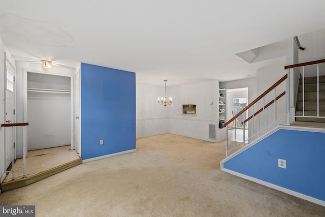 unfurnished living room featuring an inviting chandelier, stairs, a wealth of natural light, and carpet flooring