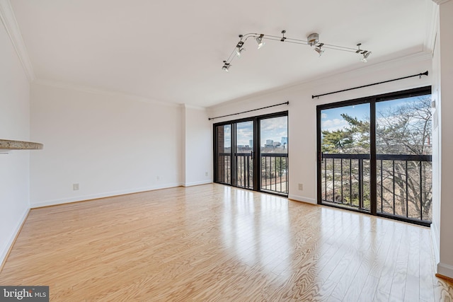 spare room with baseboards, track lighting, wood finished floors, and crown molding