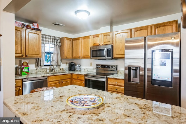 kitchen featuring visible vents, light stone countertops, brown cabinets, stainless steel appliances, and a sink