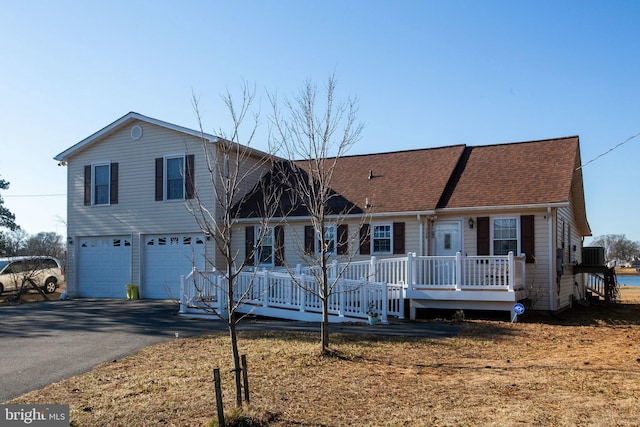 split level home featuring driveway, roof with shingles, a porch, an attached garage, and central air condition unit