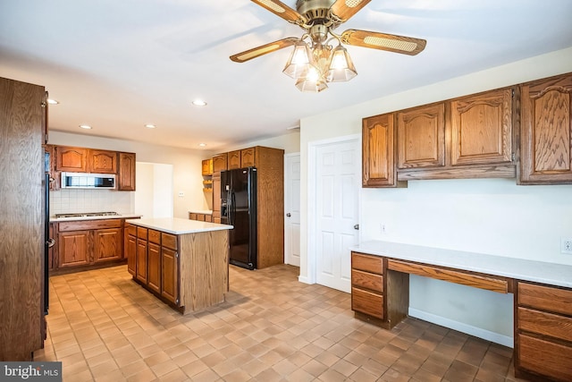 kitchen featuring brown cabinetry, appliances with stainless steel finishes, light countertops, built in desk, and backsplash