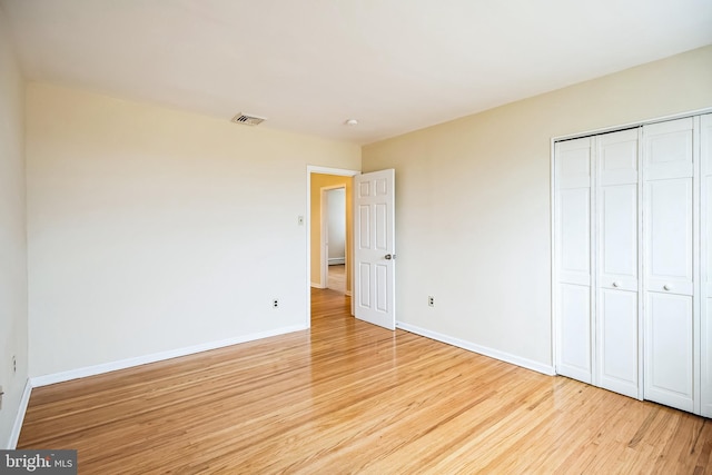 unfurnished bedroom with a closet, light wood-type flooring, visible vents, and baseboards