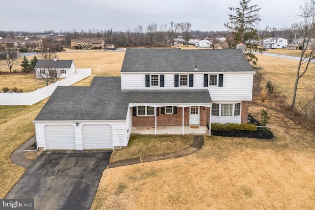 view of front of house with driveway, roof with shingles, covered porch, a front lawn, and brick siding