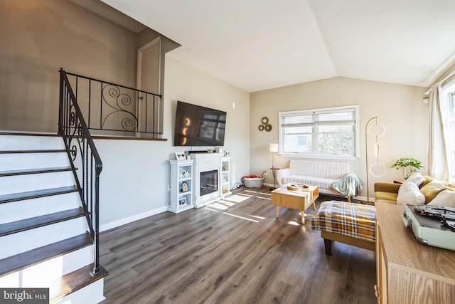 living room featuring baseboards, a glass covered fireplace, stairway, wood finished floors, and vaulted ceiling