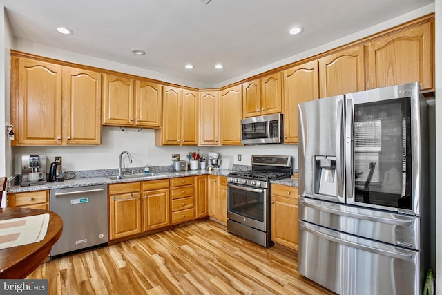 kitchen featuring appliances with stainless steel finishes, light wood-type flooring, a sink, and light stone countertops