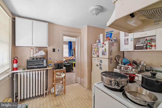 kitchen with electric stove, a toaster, radiator heating unit, freestanding refrigerator, and white cabinets