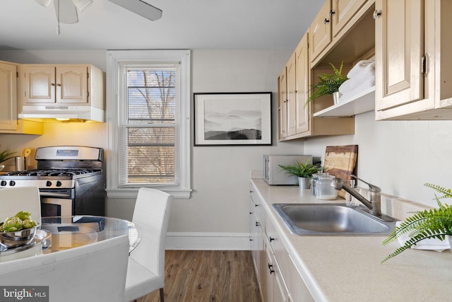 kitchen with dark wood finished floors, light countertops, stainless steel gas stove, a sink, and under cabinet range hood