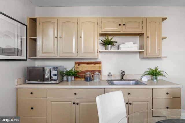 kitchen featuring a sink, stainless steel microwave, open shelves, and light countertops