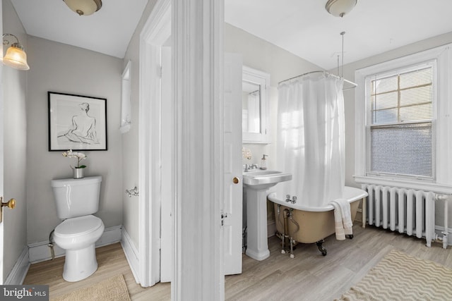 full bathroom featuring radiator, a soaking tub, toilet, and wood finished floors