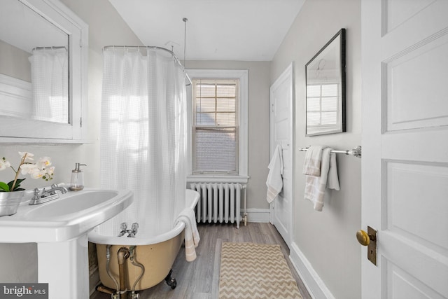 full bath featuring baseboards, a freestanding bath, radiator heating unit, and wood finished floors