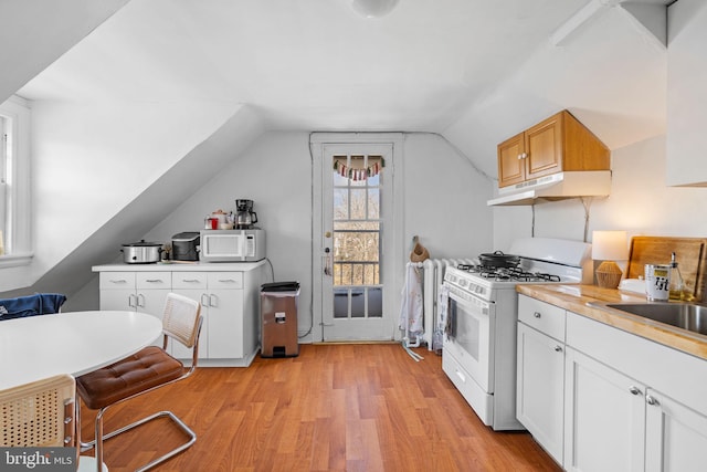 kitchen featuring light countertops, light wood-style flooring, vaulted ceiling, white appliances, and under cabinet range hood