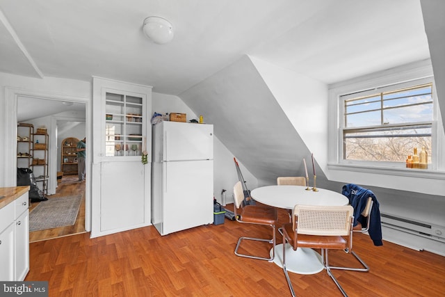 dining space with a baseboard heating unit, vaulted ceiling, and wood finished floors