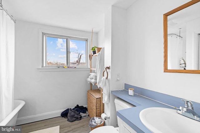 bathroom featuring baseboards, a tub, a shower with curtain, wood finished floors, and vanity