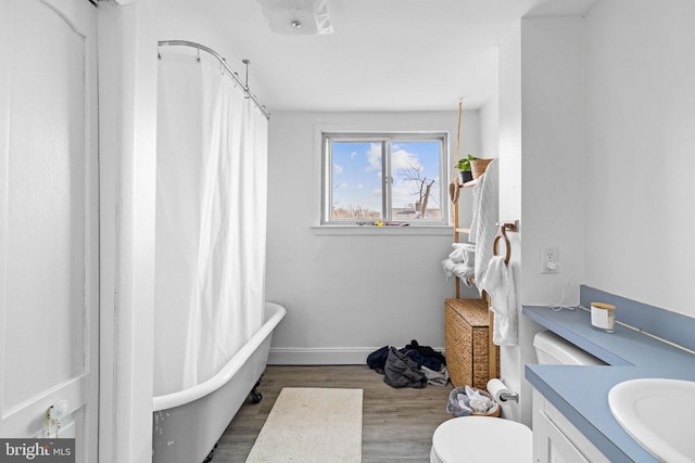 full bathroom with baseboards, toilet, wood finished floors, a freestanding bath, and vanity