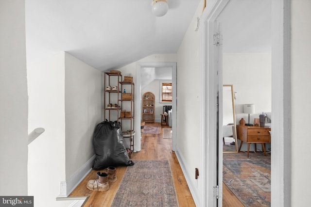 corridor with baseboards, vaulted ceiling, and light wood finished floors