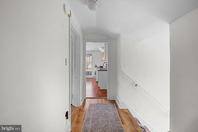 corridor featuring vaulted ceiling, light wood-style flooring, and baseboards