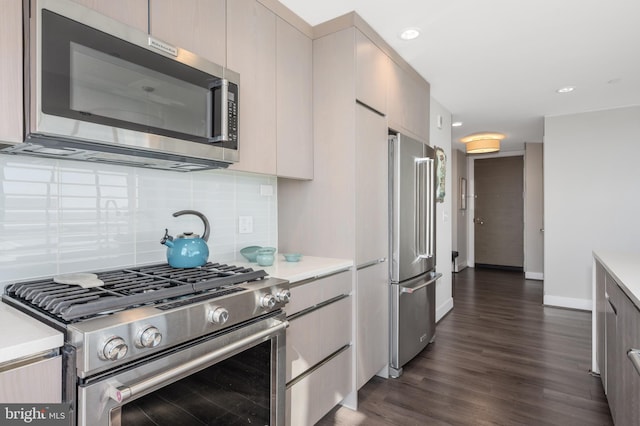 kitchen featuring dark wood finished floors, high end appliances, tasteful backsplash, light countertops, and baseboards