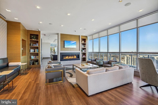 living area with a glass covered fireplace, wood finished floors, expansive windows, built in shelves, and recessed lighting