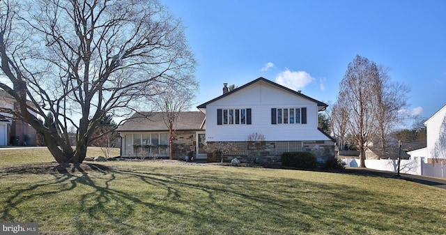 view of front of home featuring stone siding, a front lawn, a chimney, and fence