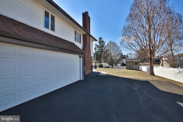 view of side of property with a garage, brick siding, fence, driveway, and a chimney