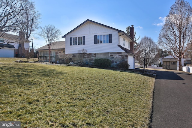 view of front facade featuring a garage, driveway, stone siding, a chimney, and a front yard