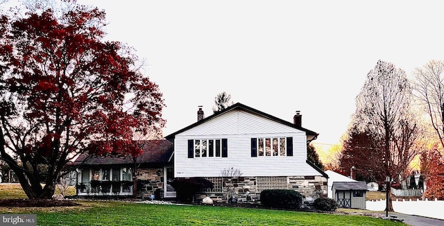 back of house with stone siding, a yard, and a chimney