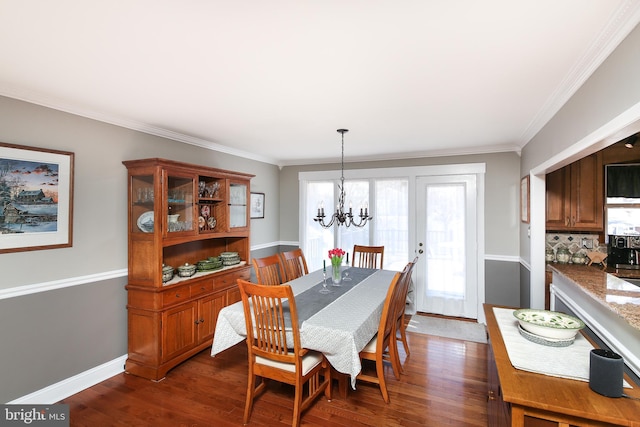 dining space featuring dark wood-type flooring, a notable chandelier, baseboards, and ornamental molding