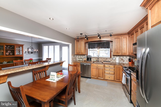 kitchen featuring decorative backsplash, brown cabinetry, appliances with stainless steel finishes, light stone counters, and an inviting chandelier