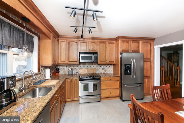 kitchen with stone counters, stainless steel appliances, a sink, backsplash, and brown cabinetry