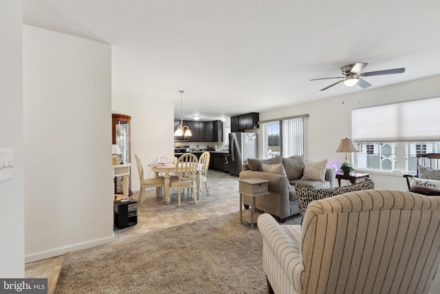 living area featuring light colored carpet, ceiling fan, and baseboards