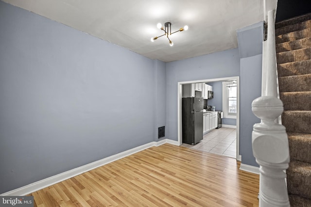 unfurnished room featuring visible vents, stairway, light wood-style floors, a chandelier, and baseboards