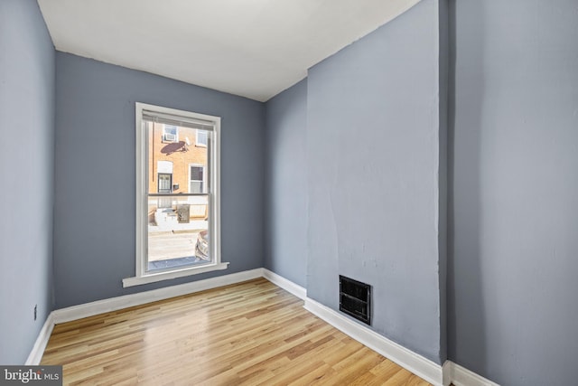 empty room with light wood-style flooring, a fireplace, visible vents, and baseboards