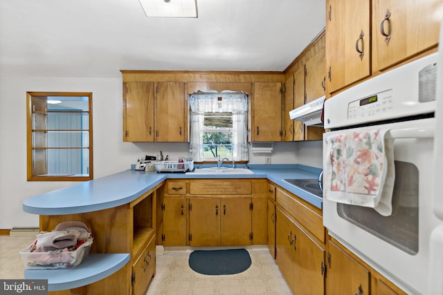 kitchen featuring under cabinet range hood, light floors, light countertops, white oven, and a sink