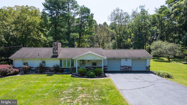 ranch-style house featuring a front yard, a chimney, a garage, stone siding, and aphalt driveway