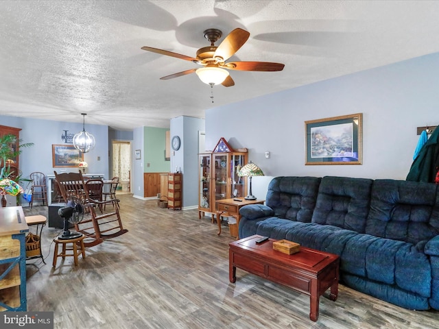 living room with ceiling fan with notable chandelier, a textured ceiling, and wood finished floors