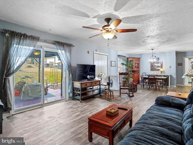 living area with ceiling fan with notable chandelier, a textured ceiling, and wood finished floors