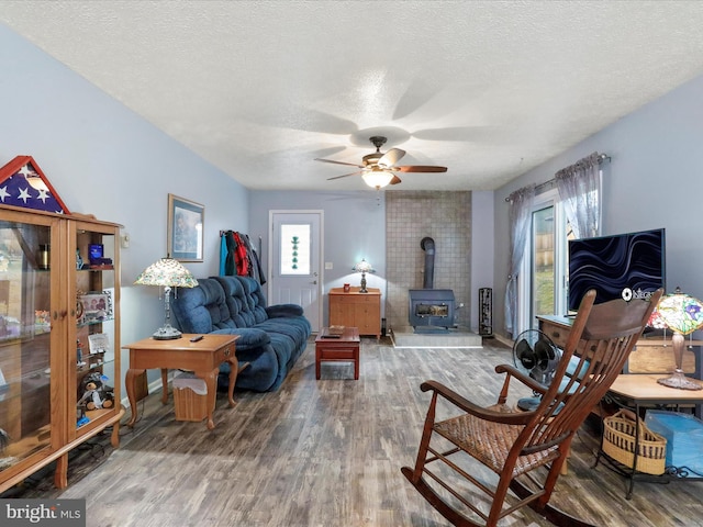 living area featuring a wood stove, plenty of natural light, a textured ceiling, and wood finished floors