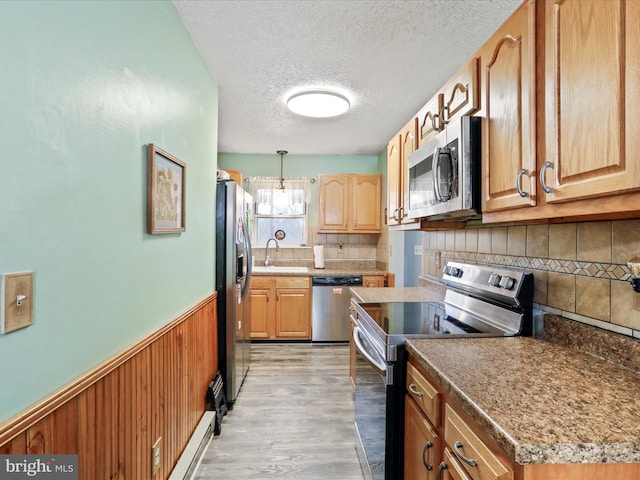 kitchen featuring a textured ceiling, a sink, light wood-style floors, appliances with stainless steel finishes, and wainscoting