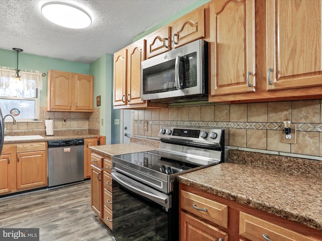 kitchen with light wood finished floors, tasteful backsplash, appliances with stainless steel finishes, a sink, and a textured ceiling