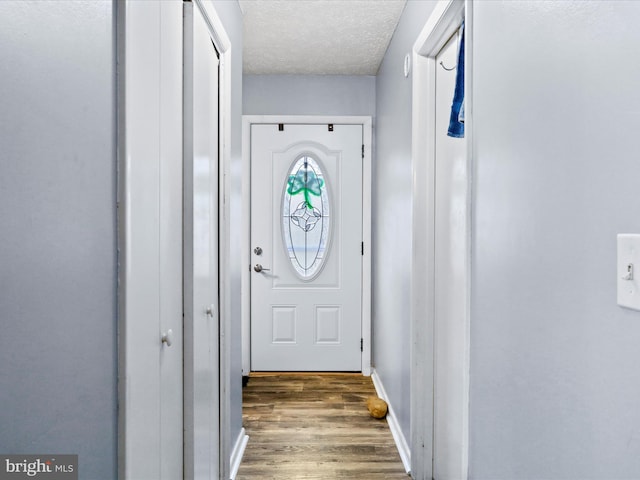 doorway with a textured ceiling, wood finished floors, and baseboards