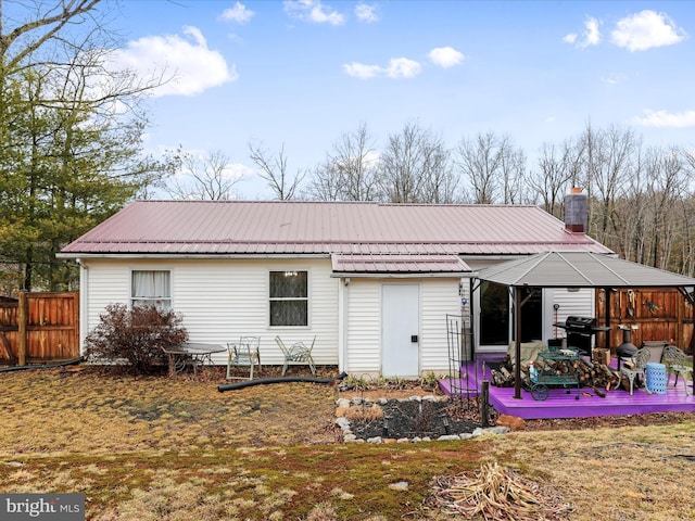 rear view of house featuring a chimney, fence, metal roof, and a gazebo