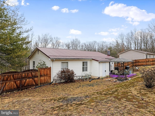 rear view of property with a chimney, fence, and metal roof