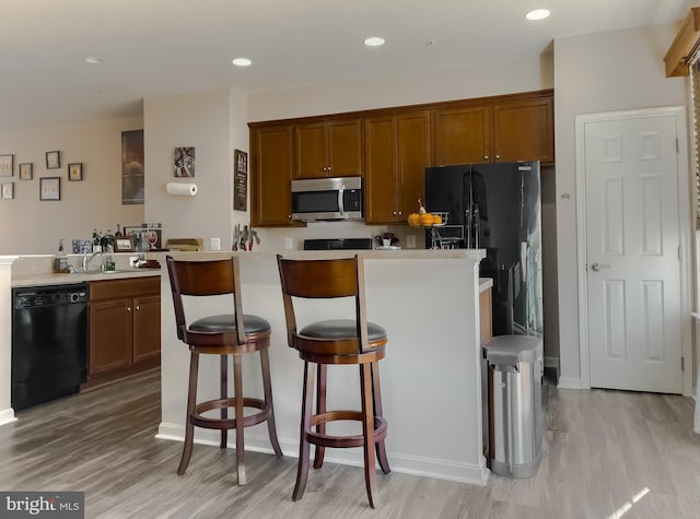 kitchen featuring light wood-style floors, light countertops, black appliances, brown cabinetry, and a kitchen bar