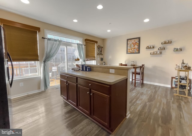 kitchen with light wood-type flooring, a center island, freestanding refrigerator, and baseboards