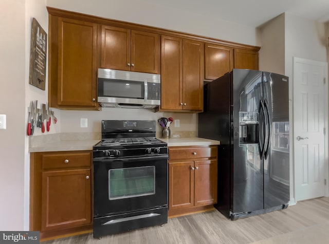 kitchen featuring brown cabinets, light countertops, light wood finished floors, and black appliances