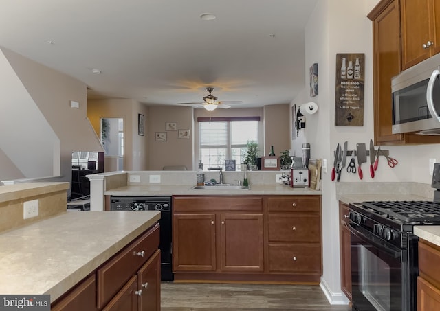 kitchen featuring a peninsula, a sink, light countertops, brown cabinets, and black appliances